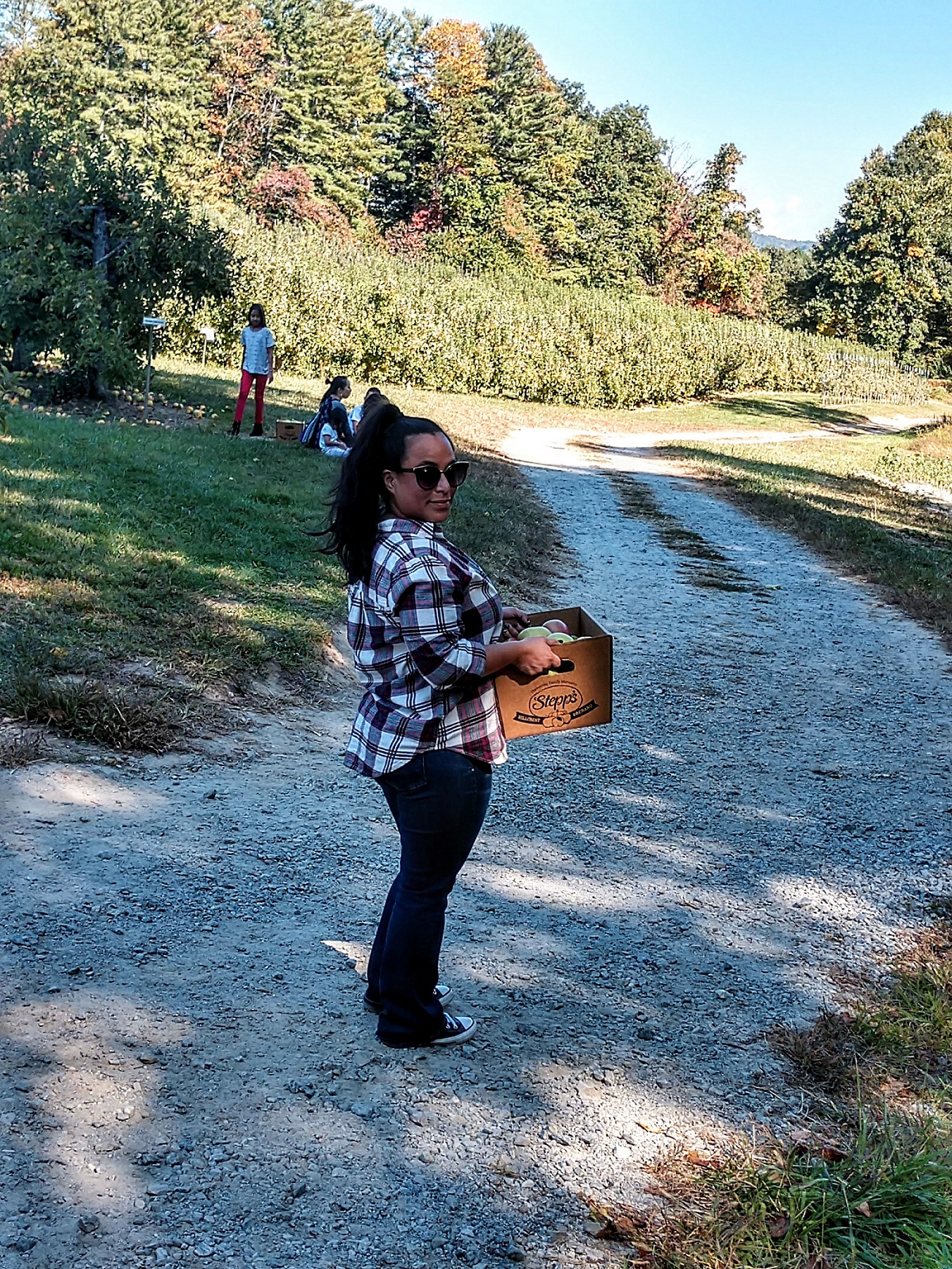 woman with a crate of apples on a gravel path